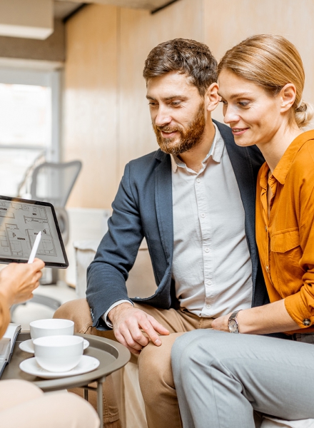 Young and lovely couple choosing a new house to buy, looking on the projects with a sales manager in the office of real estate agency